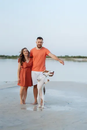 Happy couple walking with dog on beach vacation.