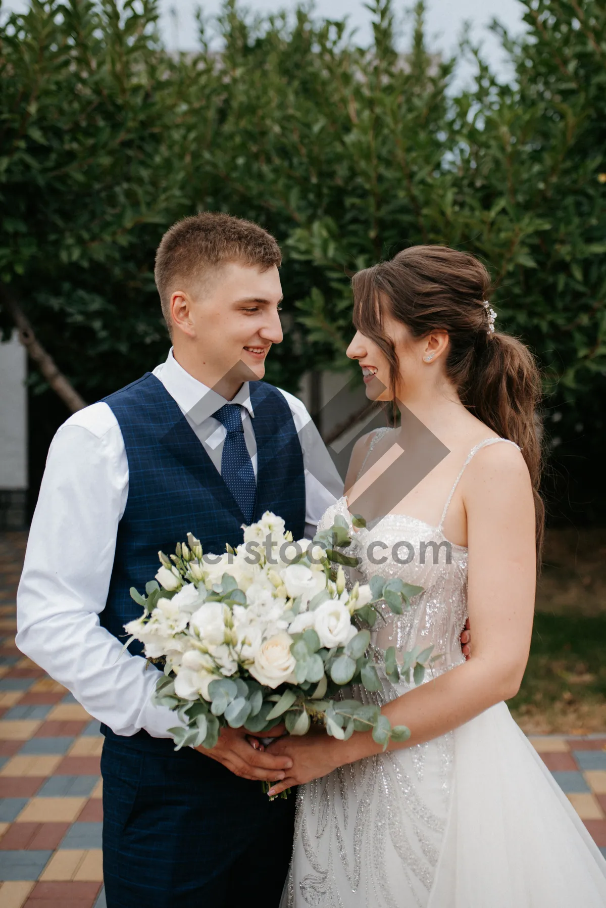 Picture of Happy wedding couple holding flower bouquet outdoors smiling together.