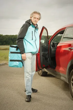 Adult man driving electric minivan with tool bag.