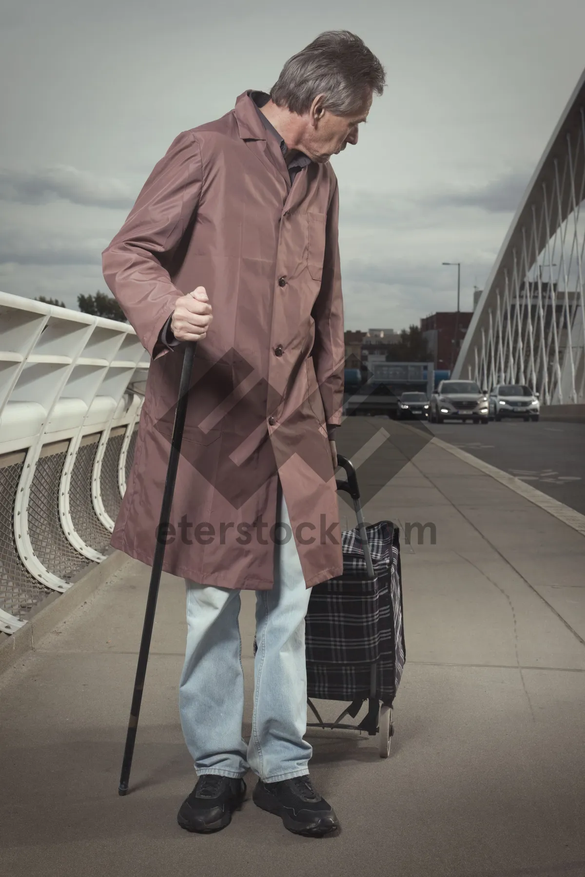 Picture of Man in trench coat with crutch on street.