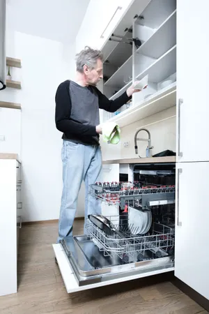 Man cooking in modern kitchen with dishwasher appliance.