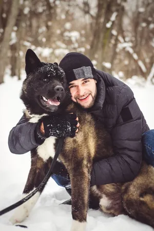 Happy person and shepherd dog playing in the snow