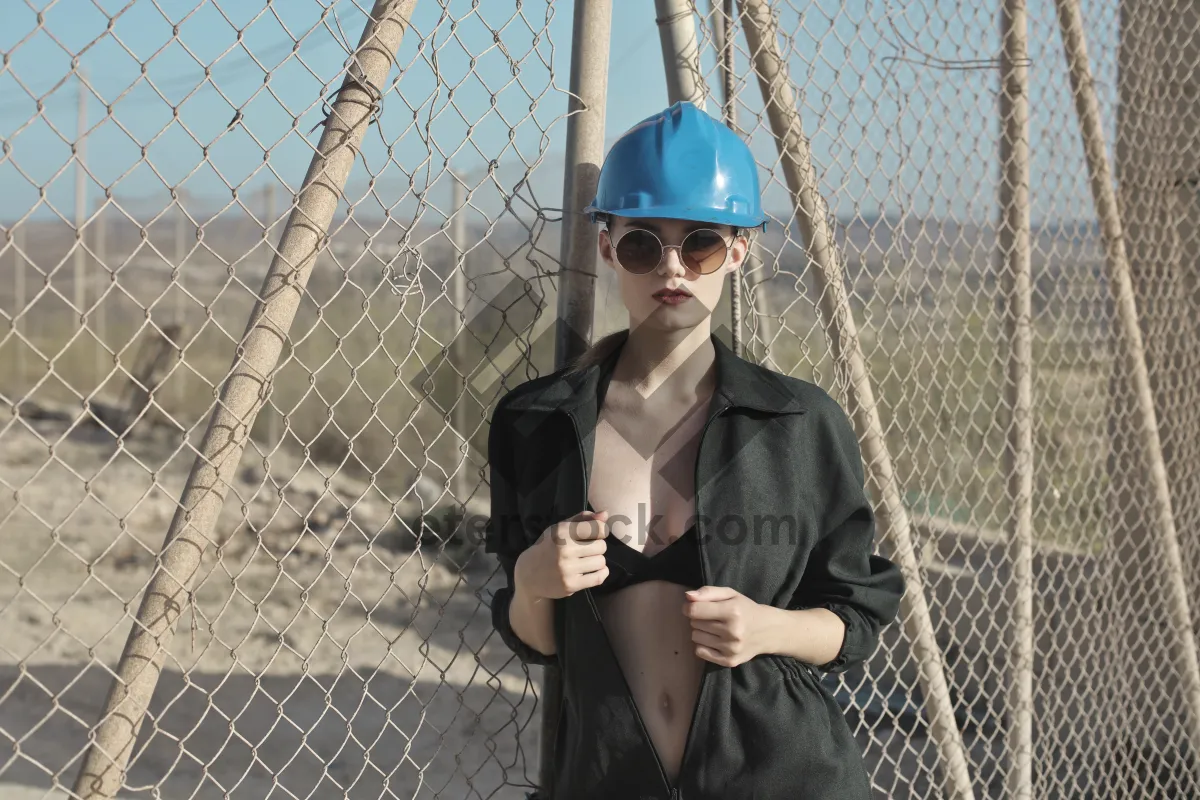 Picture of Attractive adult male at baseball batting cage fence.