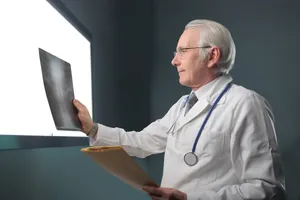 Happy male doctor working on laptop in hospital office