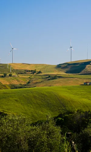 Rural mountain landscape with cloudy sky and wind turbine.