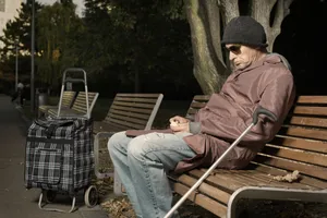 Male person sitting on park bench with crutch