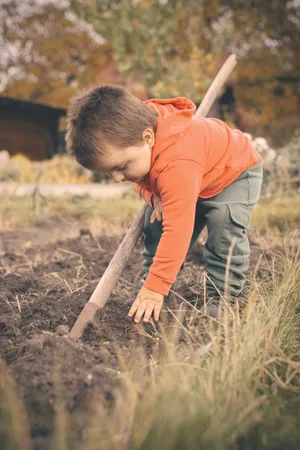 Happy farmer boy in countryside field with hoe.