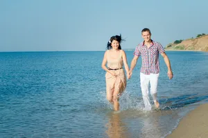 Happy couple walking on tropical beach shore in sarongs.