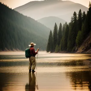 Man riding unicycle by river, surrounded by mountains.