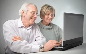 Happy elderly couple working on laptop at home