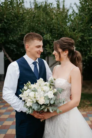 Happy wedding couple holding flower bouquet outdoors smiling together.