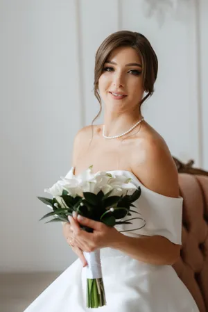 Attractive brunette bride with bouquet smiling happily in wedding dress