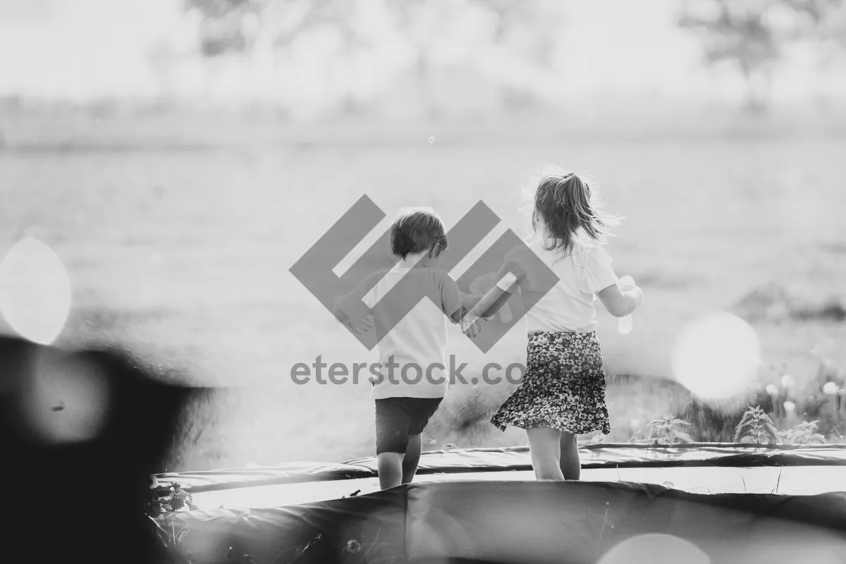 Picture of Young children lovingly play together on a trampoline in their parents' garden with a view from the living room