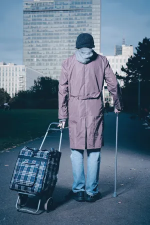 Man with crutch using shopping cart outdoors.