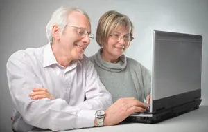 Happy senior couple working on laptop at home.