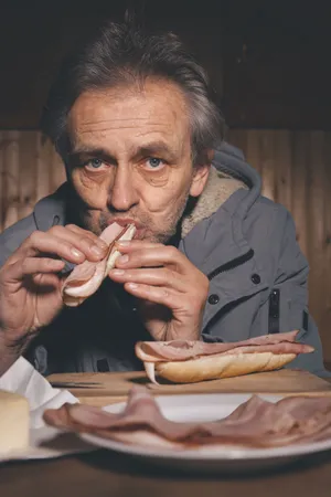 Senior man sitting at home with sandwich.